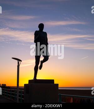 Brighton UK 1st December 2020 - The sun rises behind the statue of Olympic athlete Steve Ovett along Brighton seafront on a cold crisp morning in the south east on the first day of the meteorological winter in the UK  : Credit Simon Dack / Alamy Live News Stock Photo