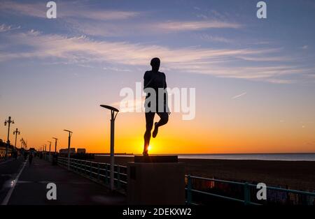 Brighton UK 1st December 2020 - The sun rises behind the statue of Olympic athlete Steve Ovett along Brighton seafront on a cold crisp morning in the south east on the first day of the meteorological winter in the UK  : Credit Simon Dack / Alamy Live News Stock Photo