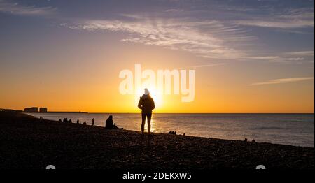 Brighton UK 1st December 2020 - Early morning walkers watch the sun rise along Brighton seafront on a cold crisp morning in the south east on the first day of the meteorological winter in the UK  : Credit Simon Dack / Alamy Live News Stock Photo