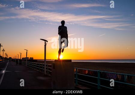 Brighton UK 1st December 2020 - The sun rises behind the statue of Olympic athlete Steve Ovett along Brighton seafront on a cold crisp morning in the south east on the first day of the meteorological winter in the UK  : Credit Simon Dack / Alamy Live News Stock Photo