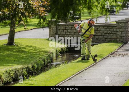 A Cormac worker strimming grass in Trenance gardens in Newquay in Cornwall. Stock Photo