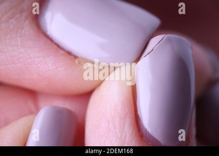 Close-up of female fingers with spoiled lilac manicure on nails Stock Photo