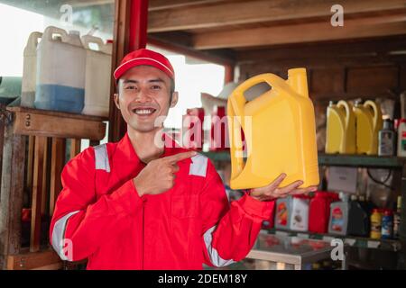 Close up of mechanic in wearpack and hat standing with finger pointing while carrying oil bottle in garage Stock Photo