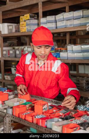 young mechanic in wearpack and hat uniform looking for parts in spare parts rack Stock Photo