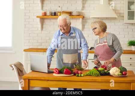 Happy senior couple watching video recipe and making healthy vegetarian meal at home Stock Photo