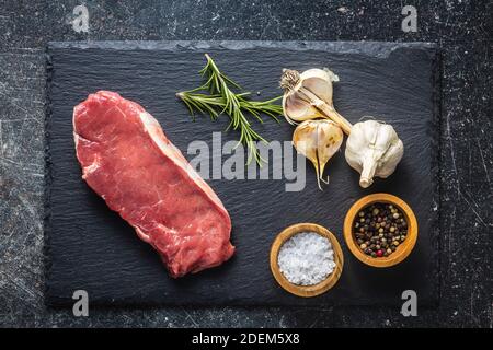 Slices raw striploin steak on a black stone cutting board. Top view. Stock Photo