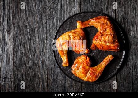 Chicken leg quarters, baked in the oven, skin-on, bone-in, served on a black plate, top view, close-up Stock Photo