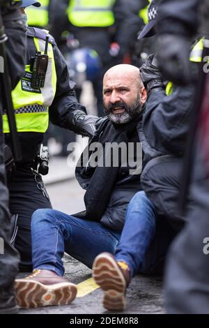 Anti-lockdown protest, London, 28 November 2020. An arrested protester sits in the road surrounded by police officers. Stock Photo