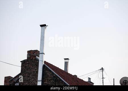 Recently renovated metal chimney and stove pipe on the roof of an individual residential house with tiles at dusk, during a sunny afternoon.  Picture Stock Photo