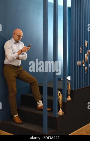 Businessman in eyeglasses looking at his mobile phone and working in office. Staying connected. Stock Photo