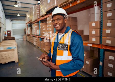Smiling portrait of a african warehouse worker holding digital tablet in hand looking at camera Stock Photo