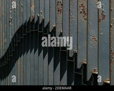 Fragment of a black fence made of strips of steel illuminated by the sun from the side. Pockets of rust on metal. Abstract image. Stock Photo
