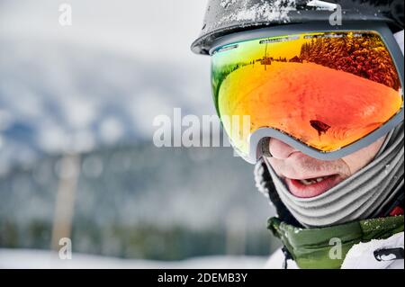 Close-up cropped snapshot of man wearing ski goggles with reflection of snowed slope. Bright glasses reflecting nature in winter. Concept of active lifestyle Stock Photo