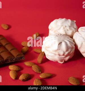 Few white delicate zephyrs with porous chocolate bar and scattering peeled almond against bright red saturated background