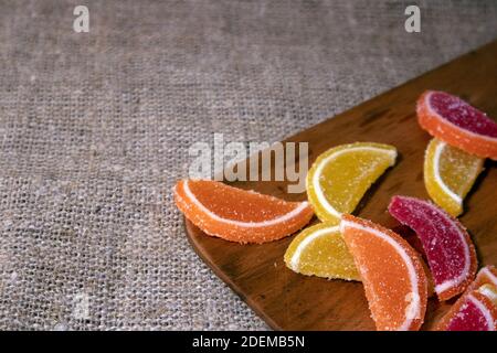 Pile of colorful candied marmalade in the shape of citrus slices lying on the sackcloth and wooden board Stock Photo
