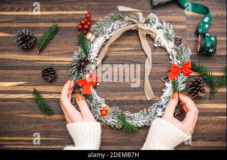 Wreath frame from pine and Christmas decor and female hands on a wooden background. Flat lay, elegant style. Christmas, New Year, preparation for the Stock Photo