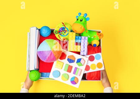 Donation concept. Hands holding donate box with clothes, books and toys on yellow background. Top view Stock Photo