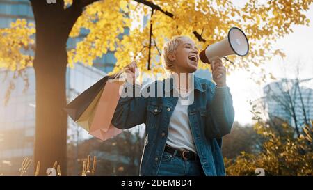 Early christmas shopping. November discounts. Blonde girl with shopping bags announcing sales season with megaphone. High quality photo Stock Photo