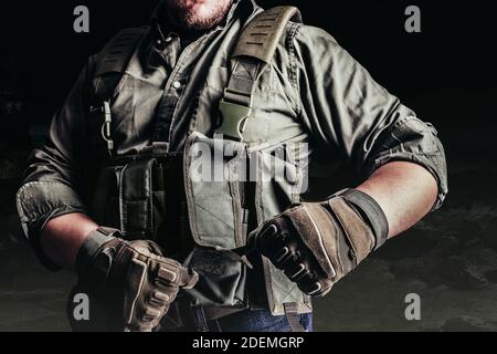 Soldier in tactical outfit and gloves putting on protective armor vest. Stock Photo