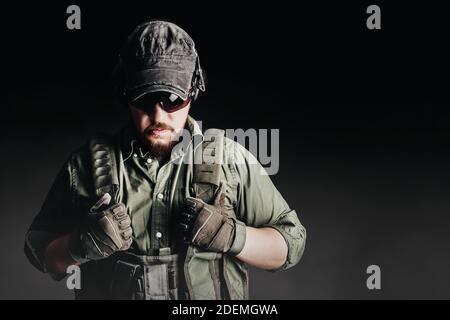 Soldier in armor vest and tactical protection outfit standing on black background with fog. Stock Photo