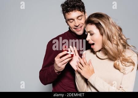 casual young man doing marriage proposal to shocked woman isolated on grey Stock Photo