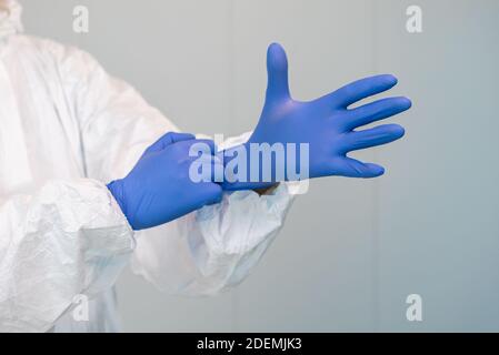 A health worker or doctor in PPE suit putting on gloves to care for patients with covid 19 or coronavirus inside hospital or clinic. Stock Photo
