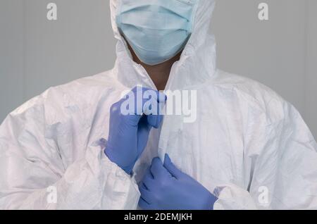 A nurse prepares by putting on protective suit during coronavirus pandemic. The nurse wears a PPE suit, gloves, and a surgical mask inside a hospital Stock Photo