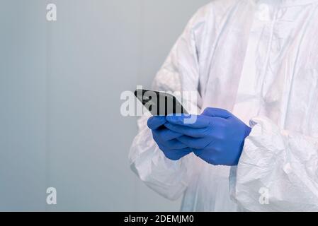 The doctor in PPE and using hand gloves consulting mobile application on smartphone during an pandemic of covid-19. Healthcare worker in personal prot Stock Photo