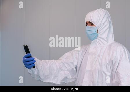 The doctor on PPE using hand gloves and consulting mobile application on smartphone during an pandemic of covid-19. Healthcare worker in personal prot Stock Photo
