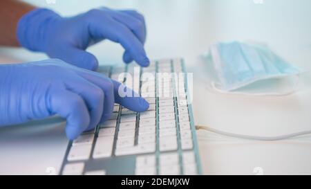 Nurse typing on a keyboard with both hands in a hospital consultation. Mask near the keyboard. Prevention of Coronavirus or Covid 19. Stock Photo