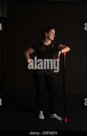 Fitness woman leans on bodybar stretches her arms. Go in for sports on a black background with a kind look Stock Photo