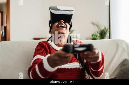 Senior african woman playing console games wearing vr headset at home during coronavirus lockdown - Focus on face