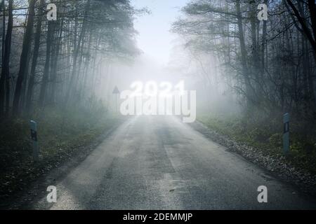 Misty country road with a blurry New Year number 2021 in the fog, leading through the forest into an uncertain future, holiday concept, copy space, se Stock Photo