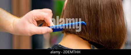 Rear view of male hairdresser combing short hair of woman in salon Stock Photo