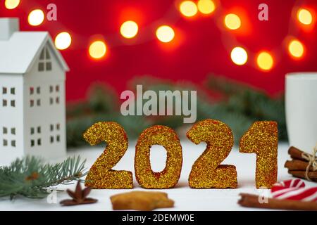 Gold glitter numbers 2021 with white house, mug and bokeh on red background. Merry christmas and a happy new year. Stock Photo