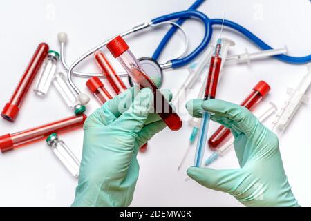 lab technician assistant holding syringe and test tube over light grey or white background with medical ampoule vials, syringes and stethoscope Stock Photo