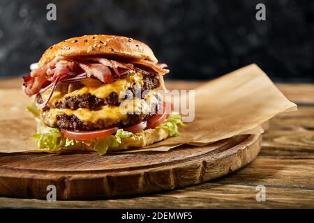 A large mouth-watering burger with grilled beef patty and fresh vegetables. Tasty american cheeseburger on a wooden board. Classic homemade burger in Stock Photo