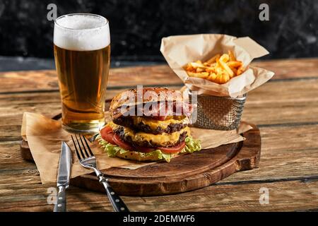 A large mouth-watering burger with grilled beef patty and fresh vegetables. Tasty american cheeseburger on a wooden board. Classic homemade burger in Stock Photo