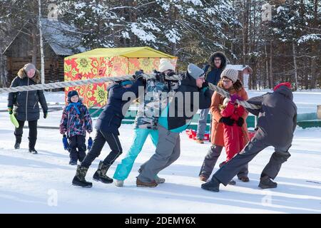 Irkutsk, Russia- 8 January 2019: Happy people having fun playing tug-of-war in winter park of Ethnographic museum Taltci. Stock Photo