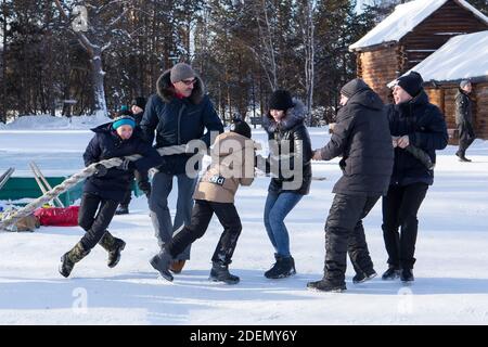 Irkutsk, Russia- 8 January 2019: Happy people having fun playing tug-of-war in open air in Ethnographic museum Taltci. Stock Photo