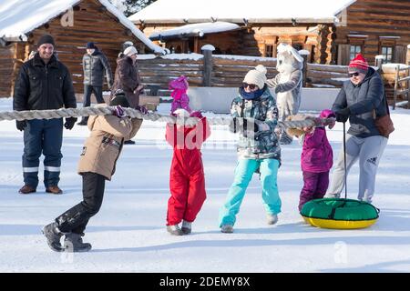 Irkutsk, Russia- 8 January 2019: Happy families with children having fun playing tug-of-war in winter park of Ethnographic museum Taltci. Stock Photo