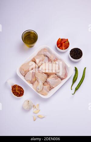 Raw chicken tender curry cut with skin arranged on white plate and garnished with garlic ,black pepper,green chilli,tomato slices,oil and chilli flake Stock Photo