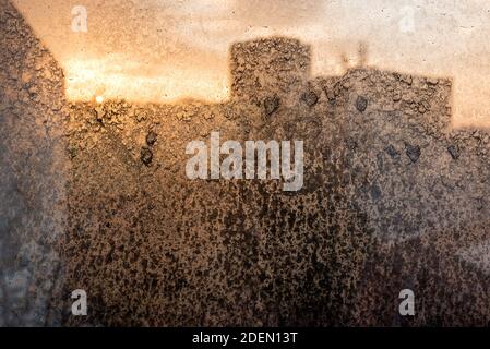 Dirty window glass with dust and dried raindrops backlit with a sunset light on a blurred background of city outlines. Dirty glass lit by the sun Stock Photo