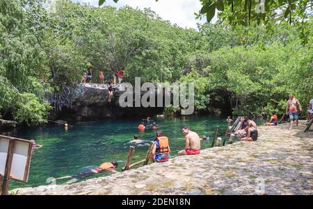 TULUM, MEXICO - Jul 29, 2019: A crowd of teenagers and families sits along the edge of the swimming area at Cenote Cristalino, a popular cenote. Stock Photo