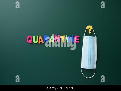 inscription quarantine from multi-colored plastic letter on a green chalk board, hanging disposable medical mask Stock Photo