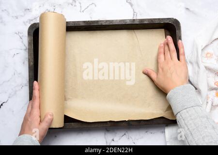 two female hands cover with brown parchment paper an iron rectangular baking sheet, top view Stock Photo