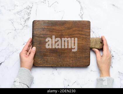 two female hands hold an empty old brown rectangular wooden cutting board, white background, top view Stock Photo