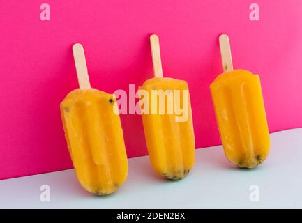 Close up of three yellow ice lollipops upside down on pink background Stock Photo