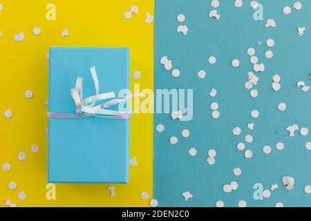 Blue gift box with ribbon and white confetti on yellow and blue background Stock Photo