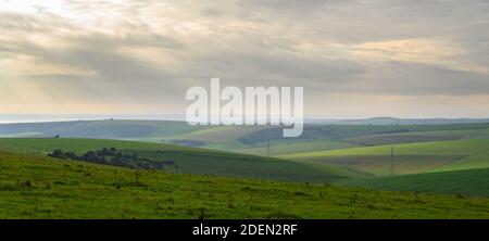 View over rolling, grassy hills to the sea in soft, wintery sunlight from South Downs Way in the Devil's Dyke area, West Sussex, England. Stock Photo